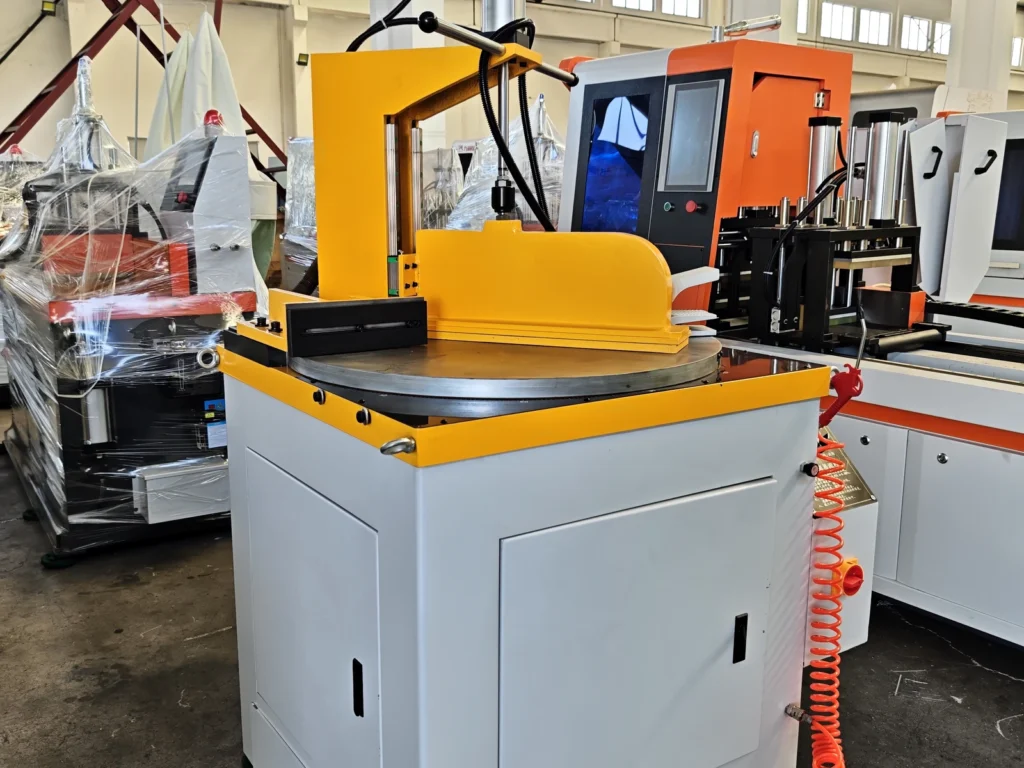 White and yellow cutting machine with a round metal worktable and upright frame among other workshop equipment.
